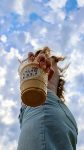 Customer holding an iced Maple and Honey coffee under a blue sky